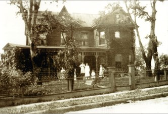 Sepia photograph of the house at 181 West Main Street in earlier years, with people standing at the front fence
