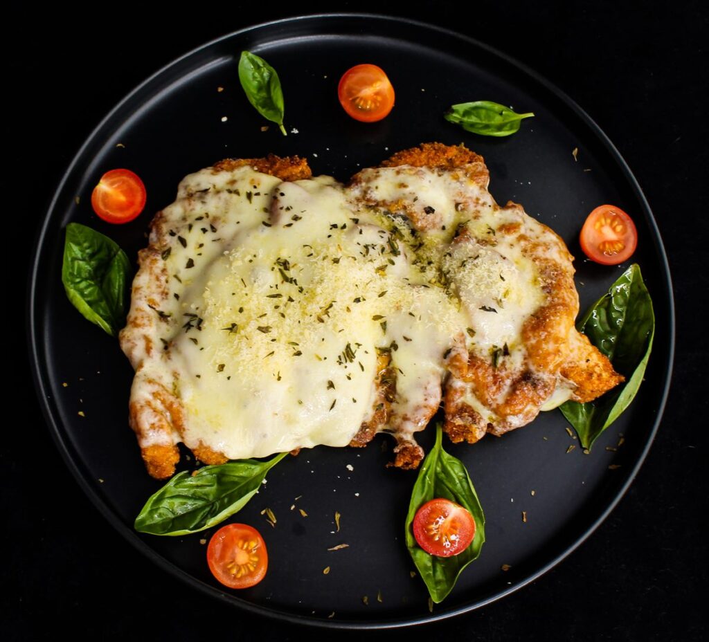 A breaded cutlet topped with melted cheese and basil