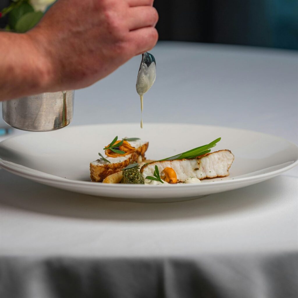 A chef finishing a plated dish with a garnish